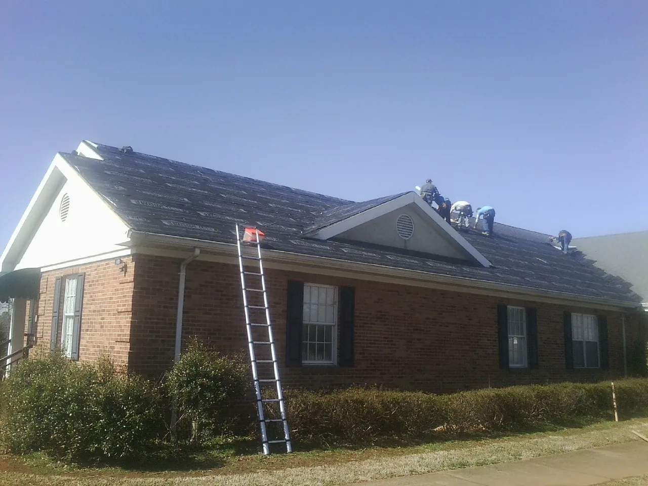 Crew tearing shingles off a brick ranch roof with a ladder set — Metal Roof Repair work by our crew in South Portland