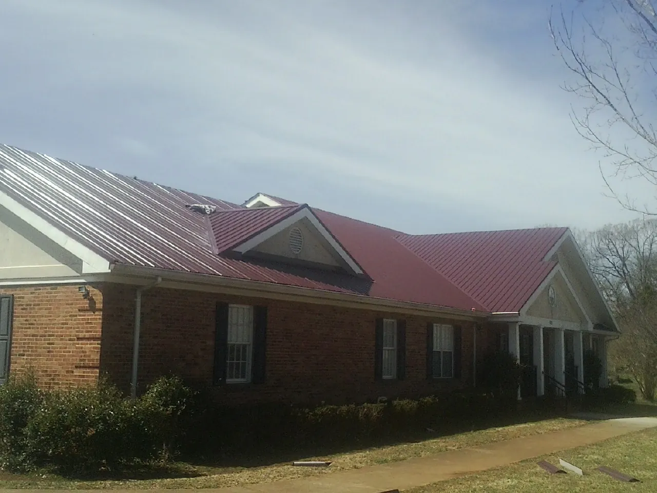 Red metal roof with gabled entries on a long brick building, from a Hail Damage Roof Repair job in South Portland
