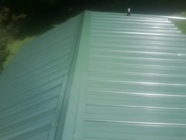 New green metal panels meeting at the ridge of a roof — Flat Roof Repair work by our crew in South Portland