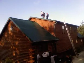 Crew on the ridge of a green metal roof on a two story log home in South Portland