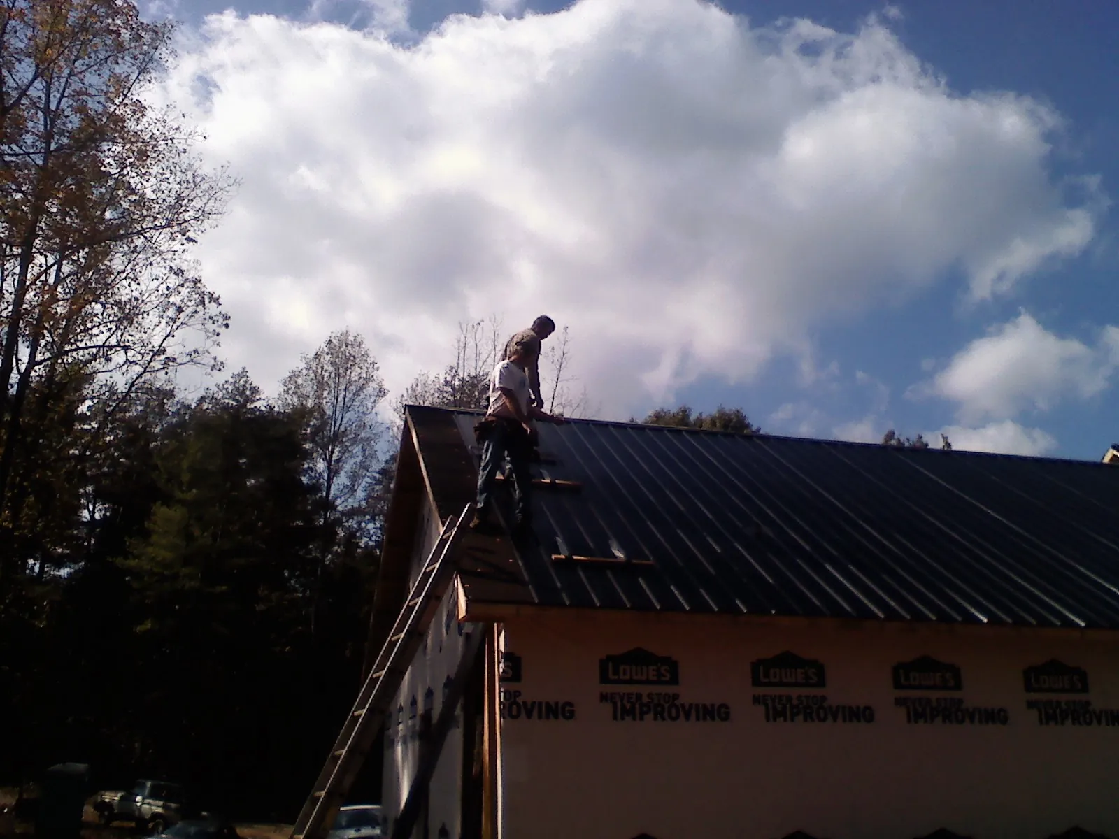 Roofer fastening dark metal panels high against a cloudy sky, from a Roof Inspection job in South Portland