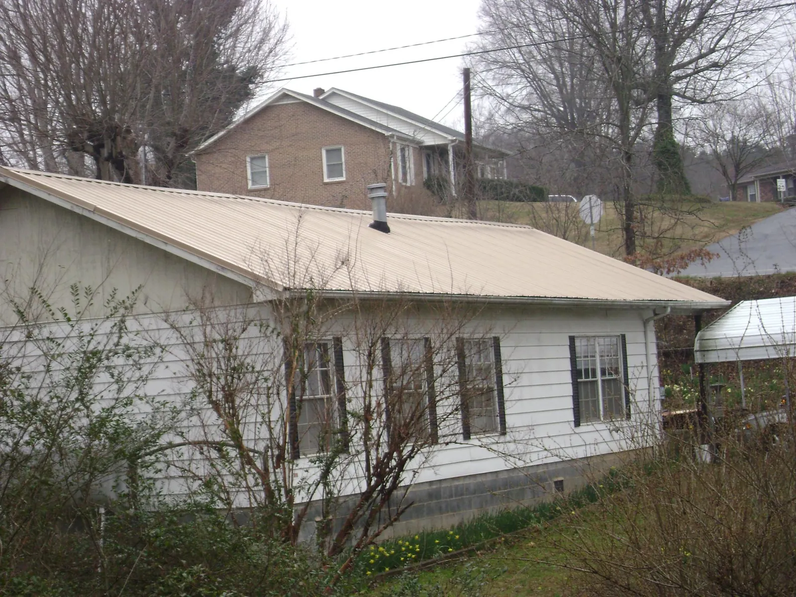 Tan metal roof on a white sided house set into a hillside — Commercial Roofing by Roofing Brothers in South Portland